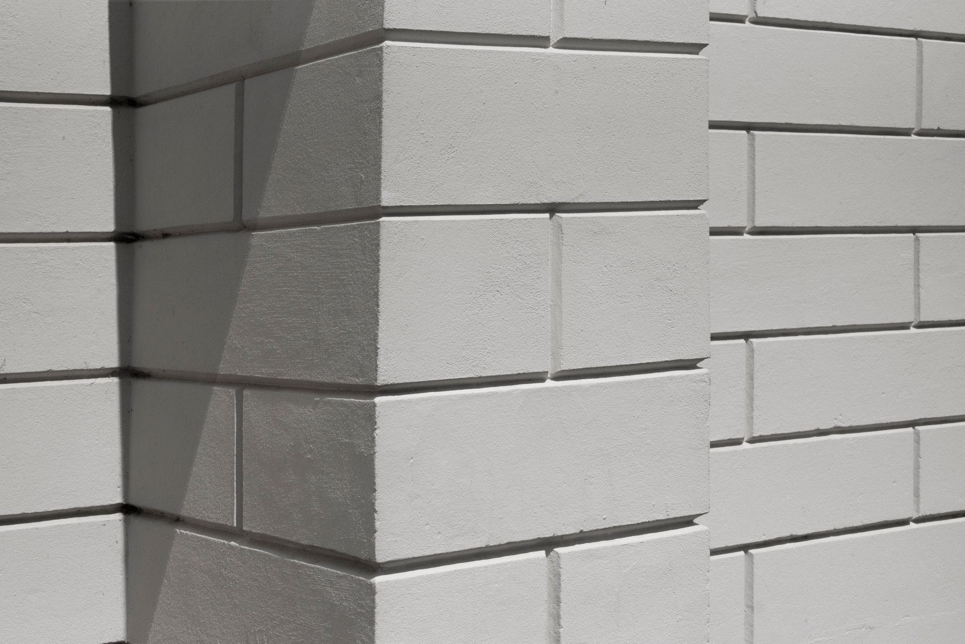Close-up of a white brick wall with geometric shadows, ideal for backgrounds.